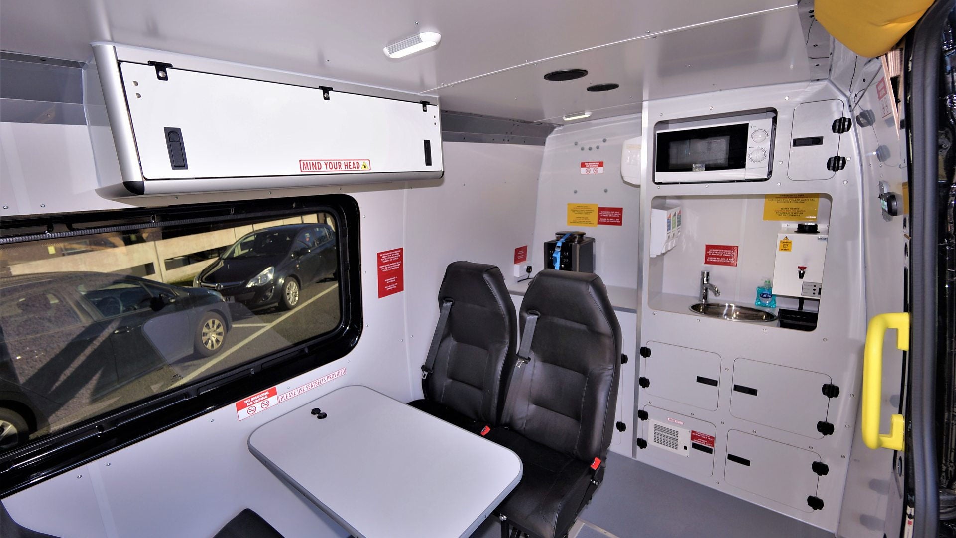 Interior of a welfare vehicle with seats, dashboard, and various equipment including a low power microwave oven.